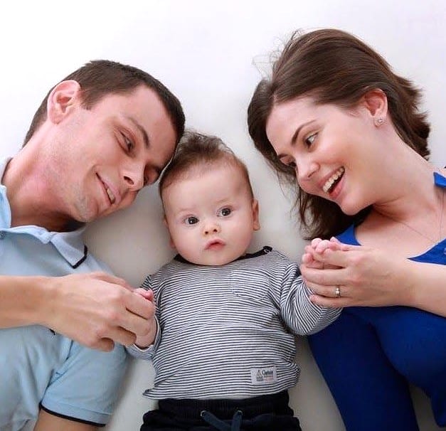 A man and woman lying on either side of a baby, smiling down at the child