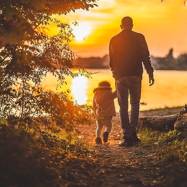Silhouette of an adult and child walking hand in hand along a lakeshore at sunset